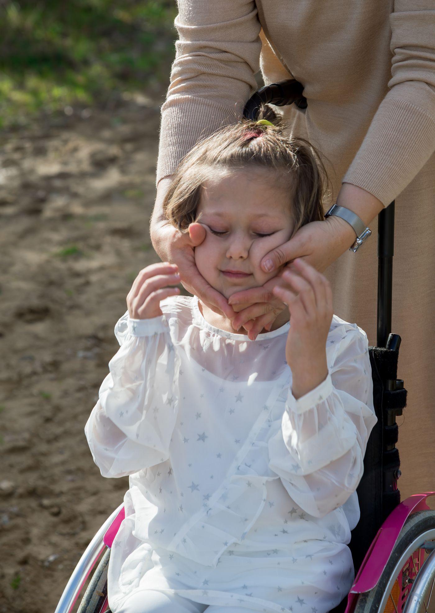 A parent gently cradling the face of their young daughter, who uses a wheelchair, as she leans into the touch with a soft smile