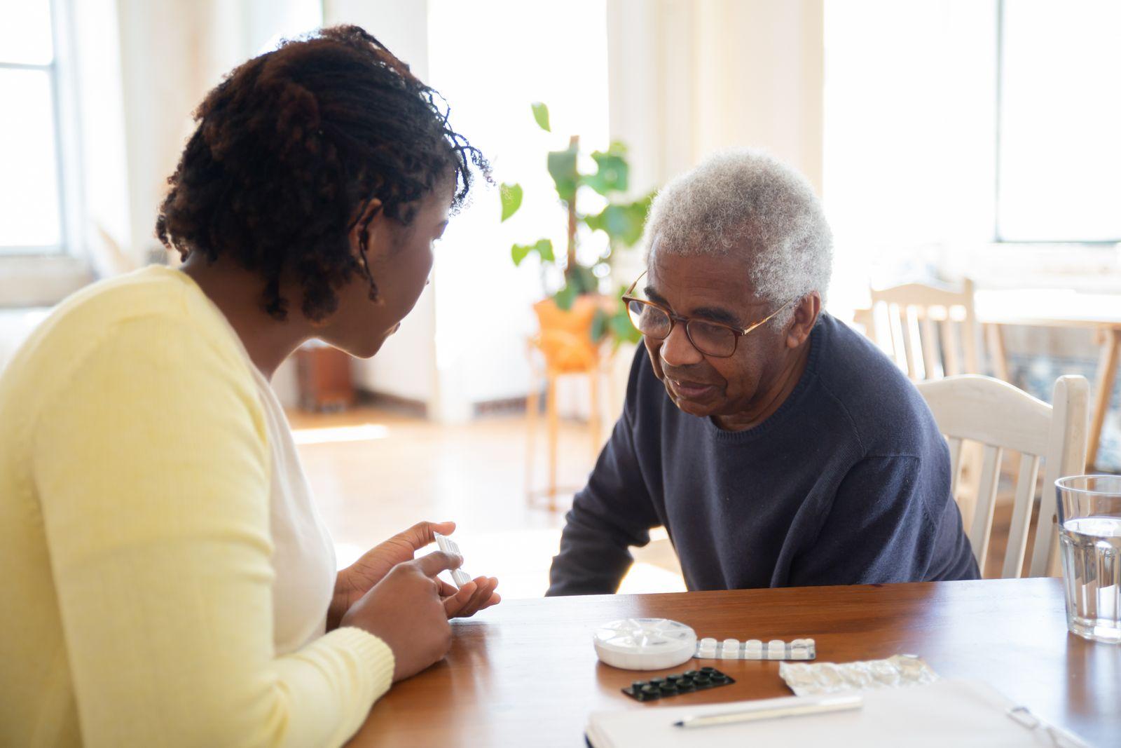 A caregiver reviewing medication with a senior man at his kitchen table