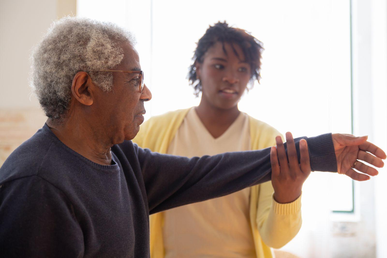 A caregiver helping a senior man with a mobility exercise at home