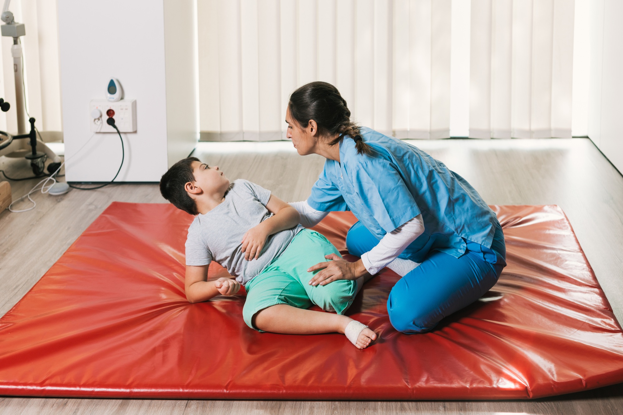 Nurse assisting child with physiotherapy exercises on red mat